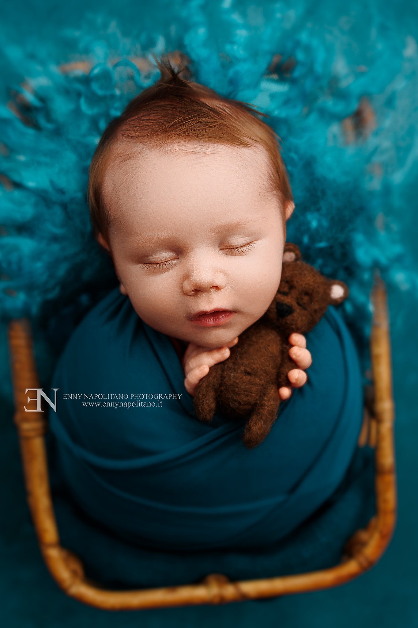 Fotografia newborn di un neonato fasciato che dorme in un prop rattan in un set color blu