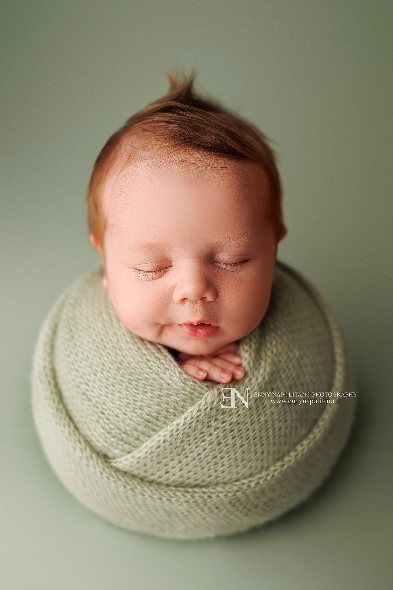 Fotografia newborn di un neonato fasciato che dorme su un set color verde salvia