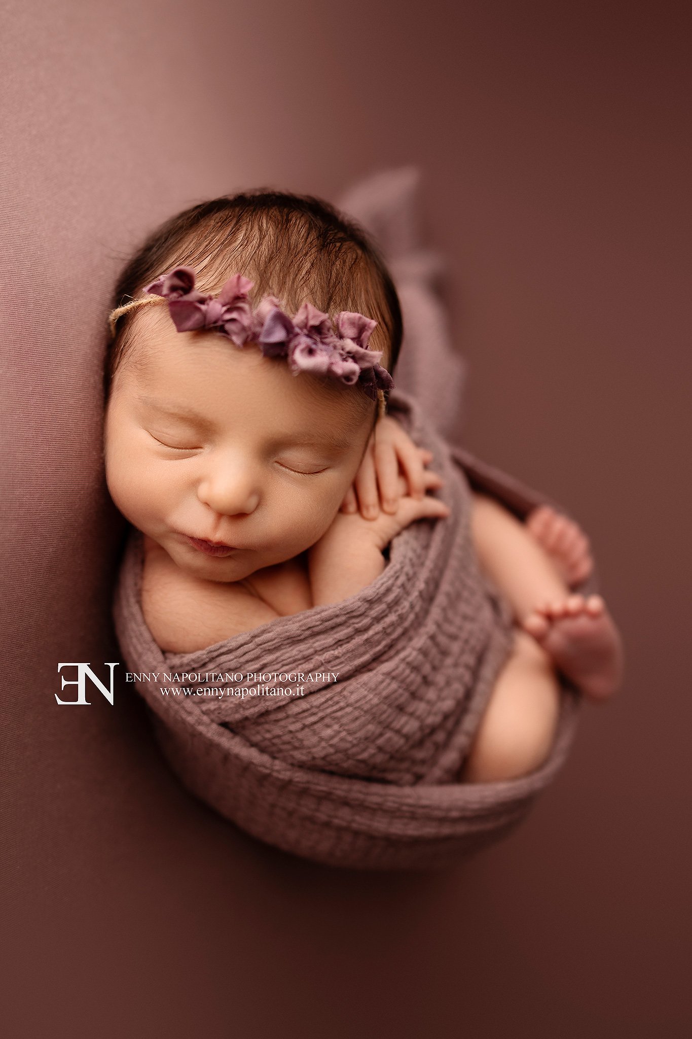 Fotografia newborn di una neonata fasciata che dorme in un set color rosa antico